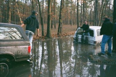 1979 Ford Bronco II - Several people attempt to free two SUVs that are stuck deep in the mud in a wooded area.