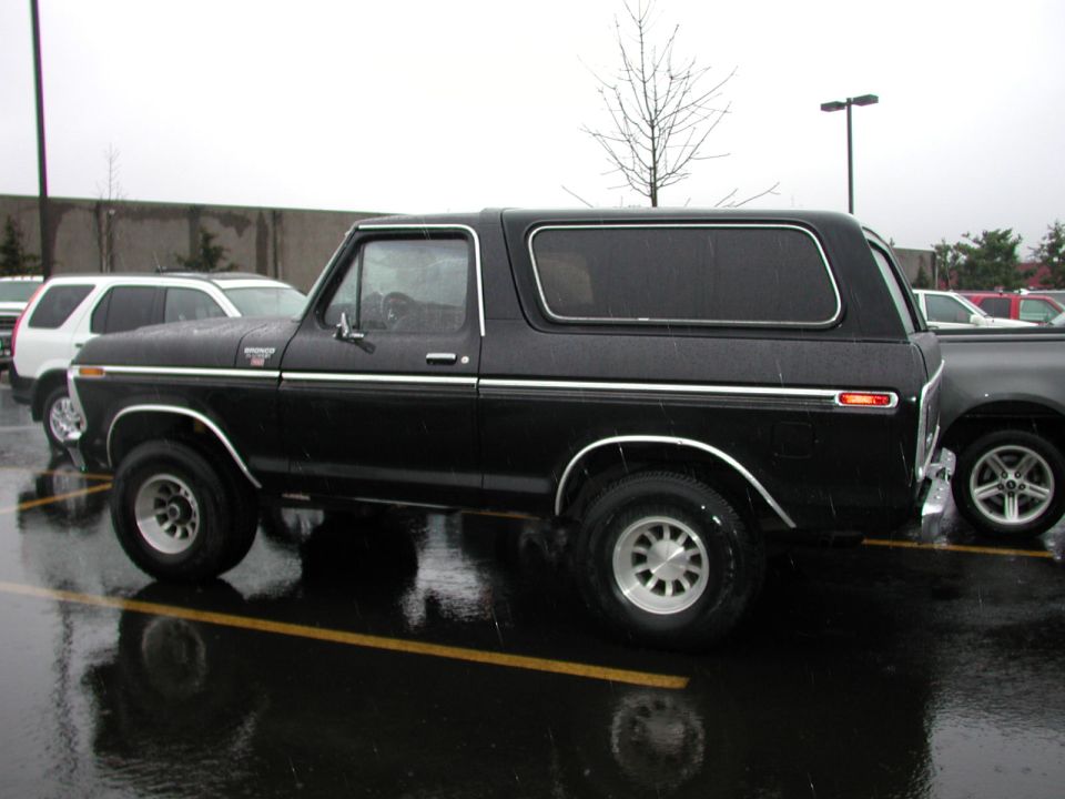 Black Ford Bronco SUV, side view, parked in a wet parking lot in the rain.