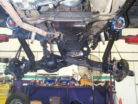 1981 Ford Bronco - Underside view of a lifted truck on a shop hoist showing the Dana 44 twin-traction-beam front axle, radius arms, differential and driveshaf…