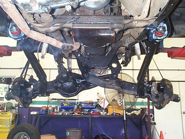 Underside of lifted truck showing TTB front axle, radius arms and coil springs on shop hoist