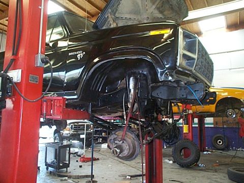 1981 Ford Bronco - Black Ford Bronco on a lift in a garage, showing its undercarriage and front end. Another vehicle is visible in the background.