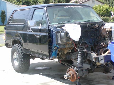 1981 Ford Bronco - Side view of a black square-body Ford Bronco in a driveway with the entire front clip, hood, fenders, grille and front wheel, removed, expo…
