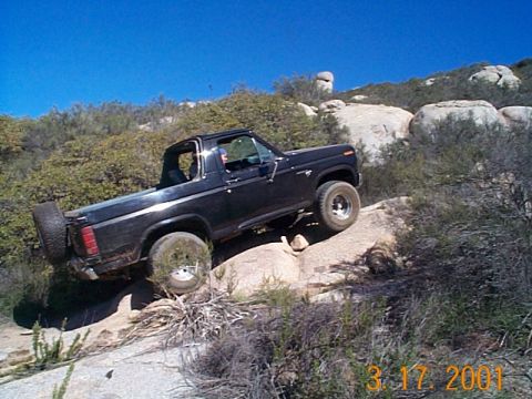 1981 Ford Bronco - A black 1981 Ford Bronco navigates a steep, rocky incline under a clear blue sky.