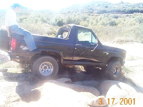 1981 Ford Bronco - A black 1981 Ford Bronco navigates a rocky trail with a person sitting in the bed.
