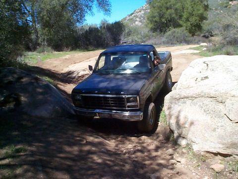 1981 Ford Bronco - This Ford pickup truck is shown driving off-road on a sunny day, with large rocks on either side of the path.