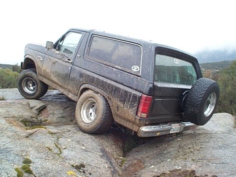 1981 Ford Bronco - A muddy Ford Bronco navigates rocky terrain from a 3/4 front angle.