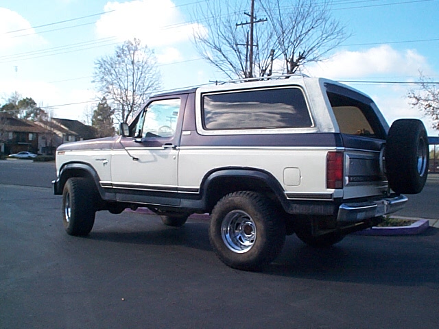 Cream and blue two-tone Ford Bronco parked on a street, rear 3/4 view with spare carrier