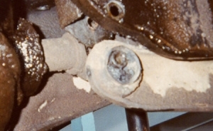 1981 Ford Bronco - Tight low-resolution close-up of a suspension or steering joint, with a light-colored ball joint or tie-rod stud and castellated nut seated…