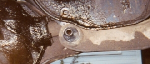 1981 Ford Bronco - Small low-resolution close-up of a rusty cast-iron housing with a threaded boss and a bolt or plug in the center, surrounded by scaly surfa…