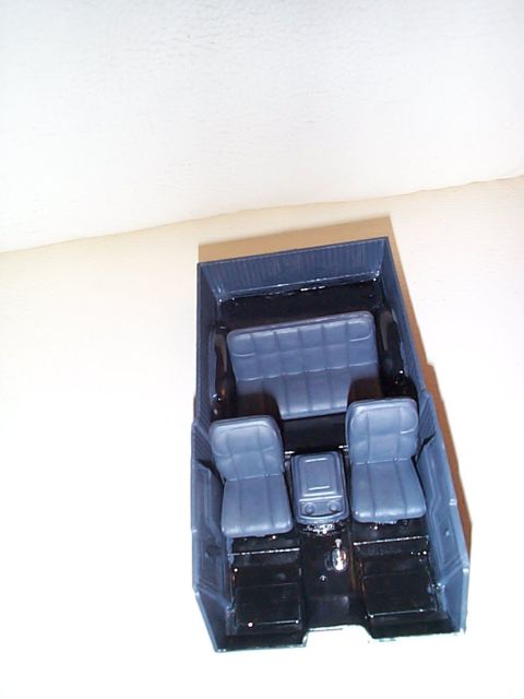 1981 Ford Bronco - Overhead view of a painted scale-model truck interior tub photographed on a plain surface, showing two gray bucket seats, a center console…