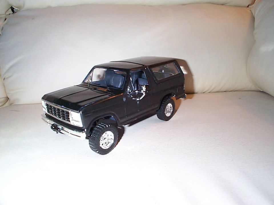 Gloss black scale model Ford Bronco with chrome grille and wheels on a white couch