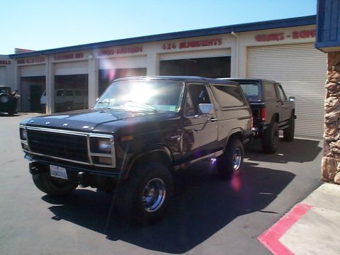 1981 Ford Bronco - Front three-quarter view of a black square-body Ford Bronco with FORD hood lettering, chrome slotted wheels, oversized all-terrain tires an…