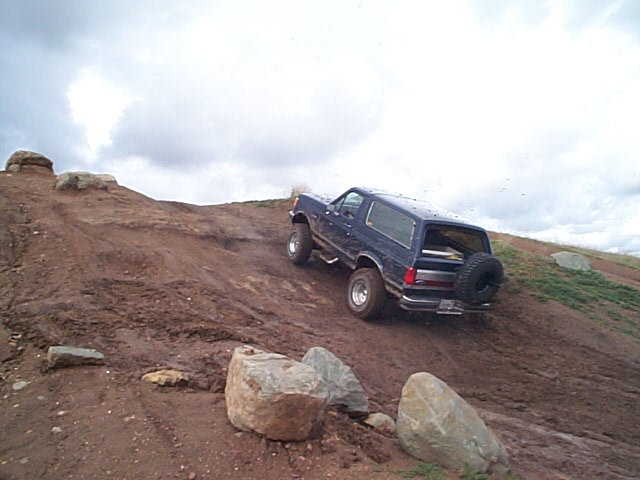 Dark blue Ford Bronco climbing a steep muddy dirt hill with rear spare tire