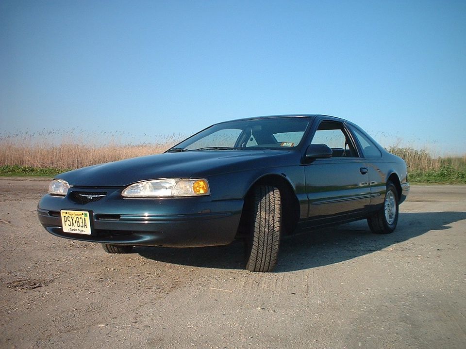 1996 Ford Thunderbird parked on a dirt road with dry grass in the background