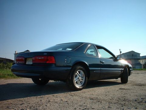 1996 Ford Thunderbird - The rear view of a dark blue coupe shows its taillights and license plate under a bright sky.