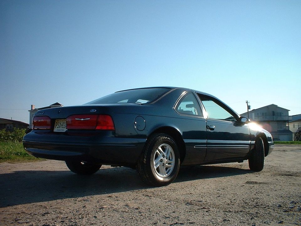 Dark blue coupe parked on a dirt lot, clear sky