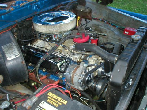 1978 Ford Bronco - Engine bay of a blue truck viewed from the driver's front corner, showing a V8 with a chrome open-element air cleaner, red distributor cap,…