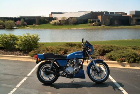 1985 Ford Crown Victoria LTD - A blue Suzuki motorcycle is parked in a lot, with a lake and office buildings visible behind it.