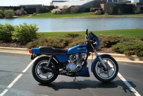 1985 Ford Crown Victoria LTD - A blue Suzuki motorcycle is parked in a lot next to a lake and a modern building.