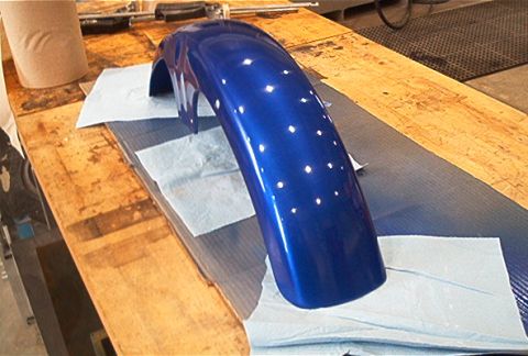 1985 Ford Crown Victoria LTD - A freshly painted blue fender sits on paper towels on a wooden workbench.