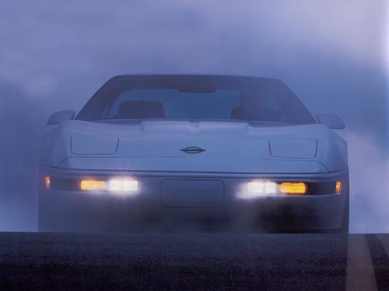 Front view of a white C4 Corvette in fog, headlights on