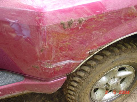 1992 Ford F-150 - Close-up of a muddy red truck's rear fender and wheel, showing signs of off-road use.