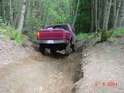1992 Ford F-150 - A red 1992 Ford F-150 navigates a challenging off-road trail through a wooded area.