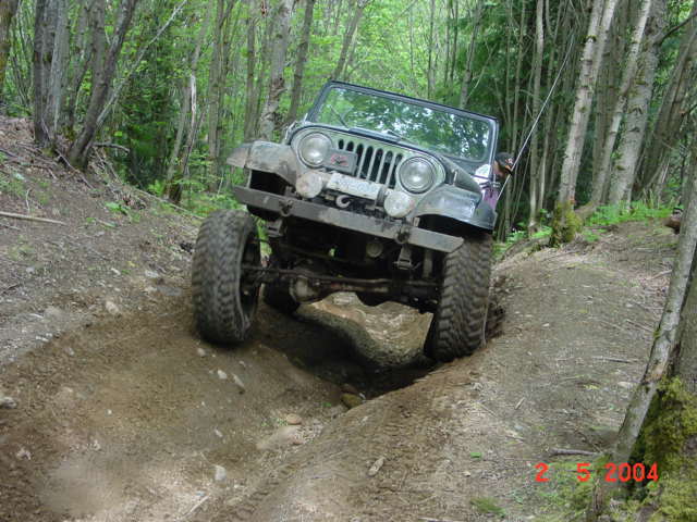 Jeep CJ-7 climbing a dirt trail in a forest