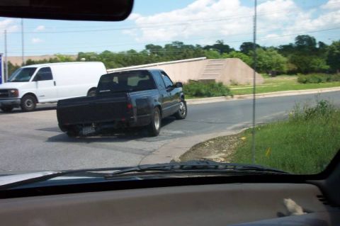 1992 Ford Bronco - A black pickup truck is seen from behind, with a white van in the distance.