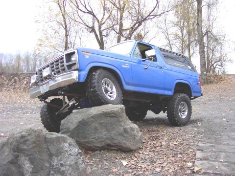 1980 Ford Bronco - This blue Ford Bronco is shown off-road, navigating large rocks with its lifted suspension.