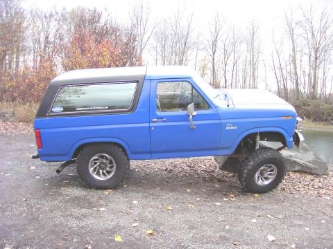 1980 Ford Bronco - This lifted Ford Bronco sits on a rocky shore, its blue paint contrasting with the black top.