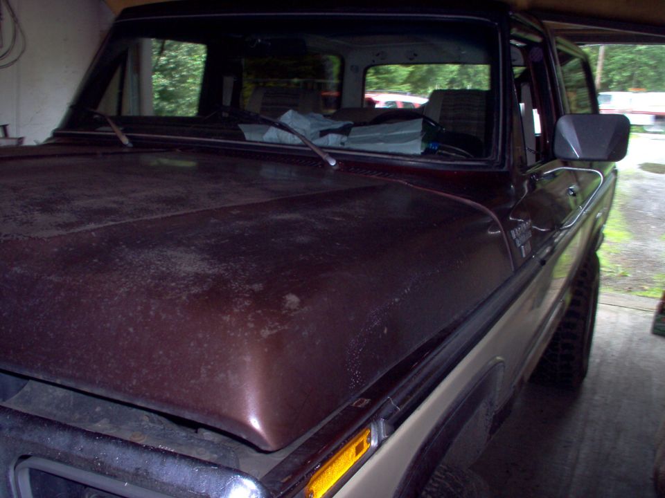 Looking across the faded maroon hood of a two-tone Ford truck parked under a carport