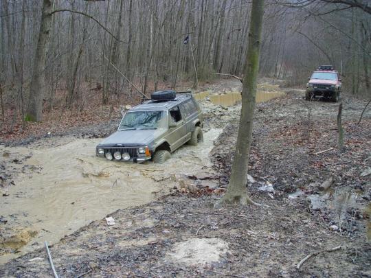 Olive green Jeep Cherokee XJ stuck in mud, another SUV behind