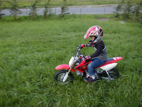 1983 Ford Bronco - A young rider navigates a grassy terrain on a red dirt bike, wearing a protective helmet and gear.