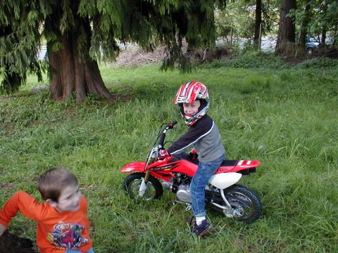 1983 Ford Bronco - A young boy in a helmet is ready to ride a red dirt bike outdoors.