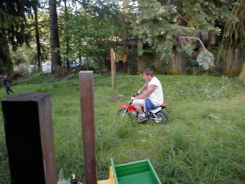 1983 Ford Bronco - A man rides a small dirt bike through a grassy area with trees in the background.