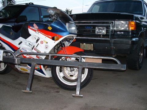 1991 Ford Bronco - A black Ford truck with a custom bumper is parked behind a white and red Honda motorcycle.