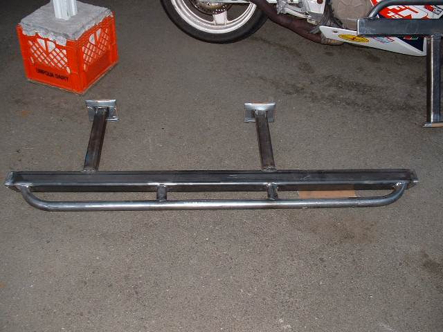 Bare fabricated steel tube bumper with mounting stingers lying on a concrete garage floor
