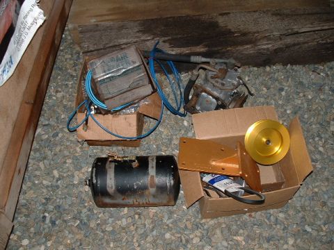 1991 Ford Bronco - Various automotive parts are laid out on a gravel surface, including an air compressor and a gold pulley.