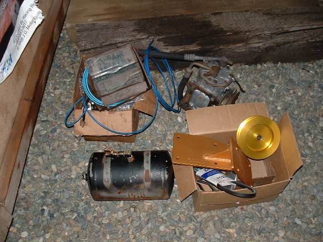 Onboard air kit on gravel: black air tank, blue air line, compressor head, gold pulley, orange bracket