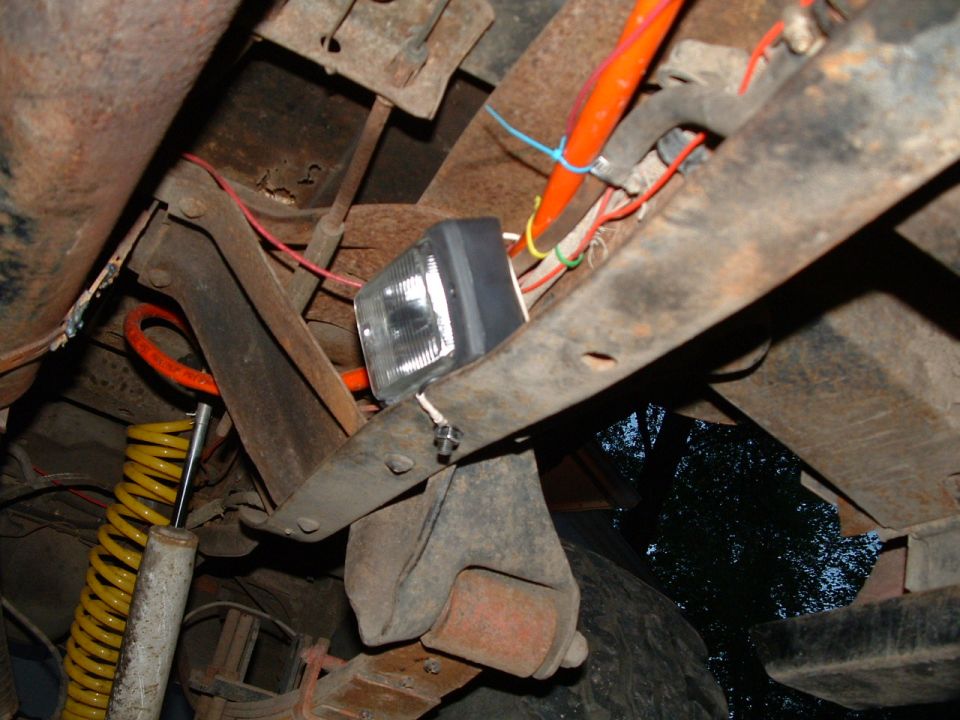 Underbody view of a square driving light mounted to a frame with colorful wiring nearby