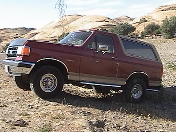 Maroon Ford Bronco SUV with tan trim, parked on dirt terrain