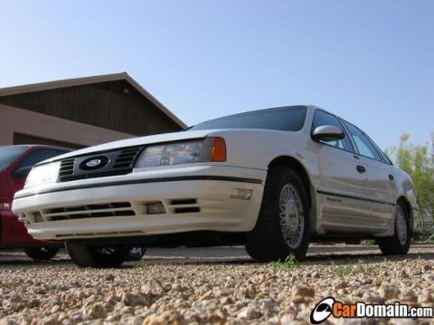 1998 Ford Taurus - A white sedan is parked on a gravel surface with a building in the background.