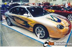 1998 Ford Taurus - A customized 1998 Ford Taurus with elaborate graphics and chrome wheels is displayed indoors.