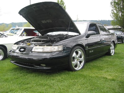1998 Ford Taurus - A black 1998 Ford Taurus is parked on grass with its hood open, revealing the engine bay.