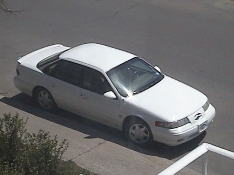 1998 Ford Taurus - A white sedan with a spoiler and aftermarket wheels is parked on the street, seen from an elevated angle.