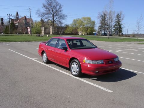 1998 Ford Taurus - A red 1998 Ford Taurus sedan is parked in a lot on a sunny day.