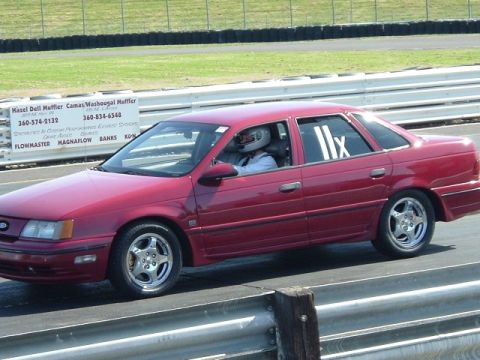1998 Ford Taurus - A red sedan, possibly a 1995 model, is on a race track with a driver in a helmet.