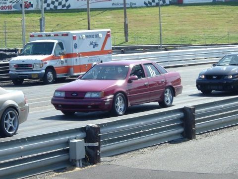 1998 Ford Taurus - A maroon sedan is on a race track, with an ambulance and other vehicles nearby.