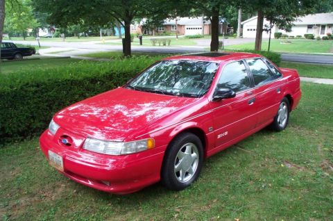 1998 Ford Taurus - A red 1998 Ford Taurus sedan is seen from a 3/4 front angle, parked on a grassy lawn.